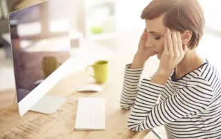 Woman sitting at a desk with fingers on her temples looking stressed.