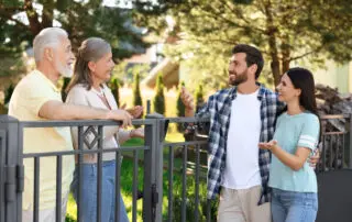 Friendly relationship with neighbours. Young family talking to a couple near fence outdoors