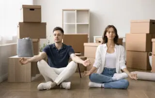 Young serene couple do meditation practice with eyes closed seated on floor on moving day, managing stress, relaxing, staying focused, maintain emotional balance on long, hard relocation, boxes nearby
