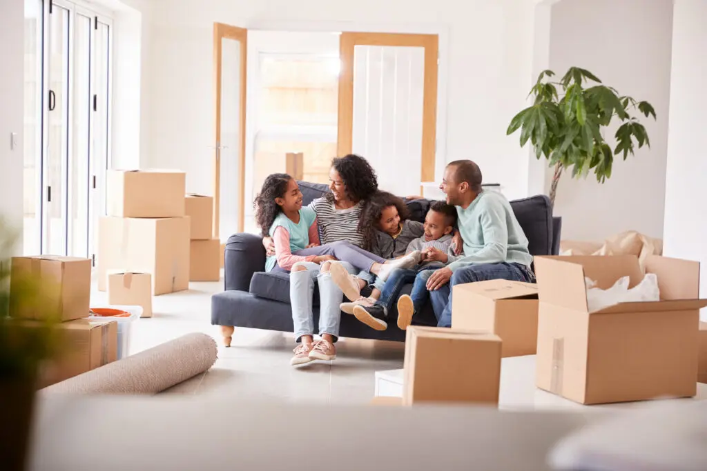 Family Taking A Break And Sitting On Sofa Celebrating Moving Into New Home Together