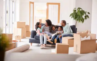 Family Taking A Break And Sitting On Sofa Celebrating Moving Into New Home Together