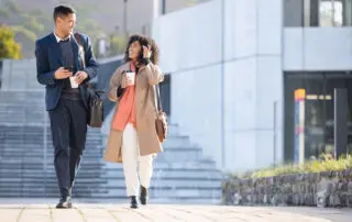 Businessman, black woman and walking with coffee in city for planning, strategy or social discussion by office building. Teamwork, finance job and friends with discussion in urban metro for success.
