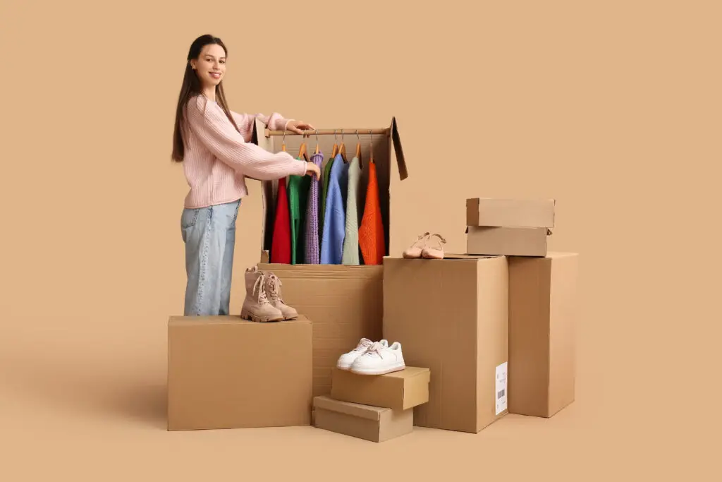 Young woman and wardrobe boxes with clothes on beige background