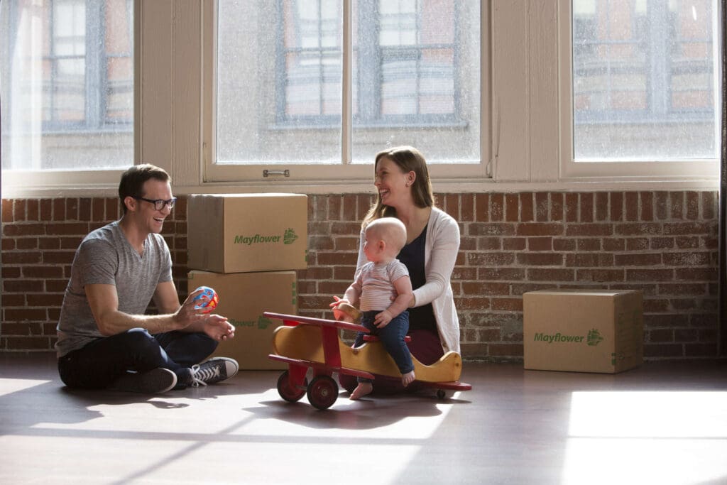 Man and woman with small child on rocking horse with moving boxes in background.