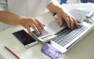 Hands at a computer, calculator, and smart phone working on a budget for moving.