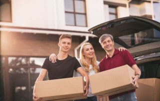 Happy family with teen son carrying cardboard boxes with their belongings, posing in front of their new home