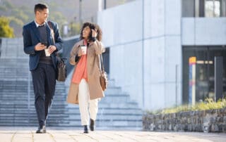 Businessman, black woman and walking with coffee in city for planning, strategy or social discussion by office building. Teamwork, finance job and friends with discussion in urban metro for success.