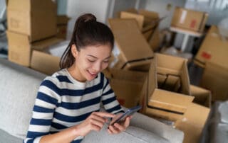 woman using cellphone mobile phone for to plan move with boxes around her