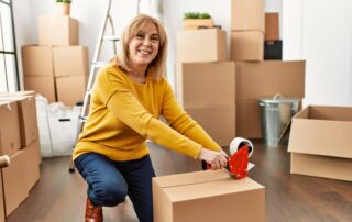 Middle age blonde woman packing box using tape at new home.