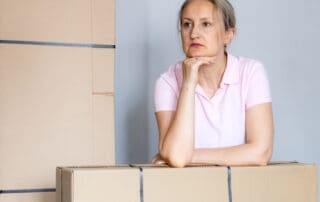 Woman leaning on moving boxes while thinking about future life changes. Relocation, emotional transition, new beginnings and uncertainty after moving to new home.