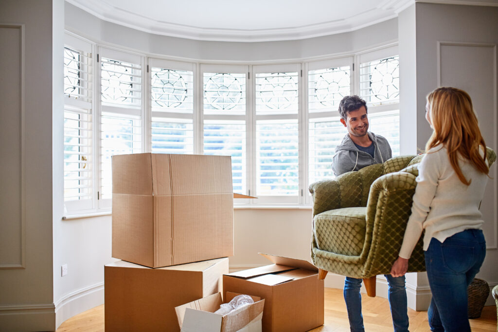 Carry, sofa and couple in new home for moving, packing furniture and relocation for real estate. Marriage, homeowner and man help woman with couch